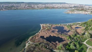 Koyu mavi Karadeniz, açık mavi bulutlu bir gökyüzünün altında geniş yeşil yolları ve büyük beton bir yol köprüsü olan bir sanayi kentini yıkıyor. UHD 4K video gerçek zamanlı