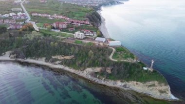 A small ancient resort town with expensive remote comfortable hotels on rocky outskirts, above a sandy vegetative wild beach near the deep blue Black Sea under a clear blue sky. UHD 4K video realtime