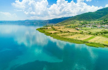 Agricultural fields planted with grain crops near small Montenegrin villages on the coast of the azure Adriatic Sea against the backdrop of peaks of the Balkan Mountains and clear cloudy sky