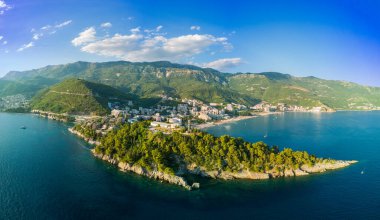 Panorama of birds eye view of historical resort towns of Budva and Becici with luxury hotels near azure calm Adriatic Sea against the backdrop of the Montenegrin Mountains and blue sky