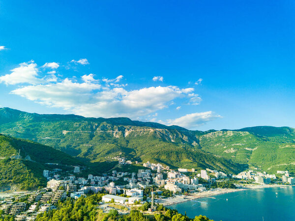 Birds eye view of historical resort towns of Budva and Becici with luxury hotels and comfortable beaches near azure calm Adriatic Sea against the backdrop of the Montenegrin Mountains and blue sky