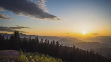 A mountain valley with mountain peaks of the Rhodope Mountains covered with dense spruce dark forests is shaded under a cloudy evening sunset bright sunny sky. UHD 4K video timelaps