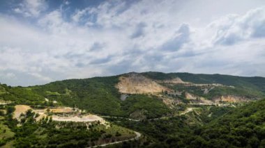 Industrial quarry for extraction of minerals with equipment and machines, and intermountain winding road passing by, in Rhodope Mountains covered with coniferous forests. UHD 4K video timelaps