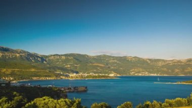 Top view of resort seaside town of Budva with various holiday hotels and fashionable beaches and boats with ships sail from coast to coast along bay in the light of setting sun. UHD 4K video timelaps