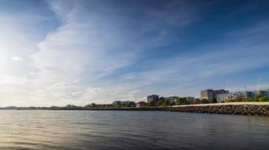 The embankment with rocky small dark stones passes over the bay of a calm deep Black sea against the backdrop of a sunset evening sunny sky. UHD 4k video timelaps