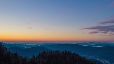 Cloudy weather over low hills covered with spruce evergreen forests in Rhodope Mountains against backdrop of sunset sky, and mystical thick white fog between mountain ranges. UHD 4K video timelaps