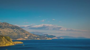 The steep slopes of the Montenegrin Mountains with resort hotels, tourist historical sites and summer green vegetation are washed by calm blue dark waters of the Adriatic Sea. UHD 4K video timelaps
