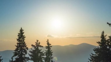 A mountain valley with mountain peaks of the Rhodope Mountains covered with dense spruce dark forests is shaded under a cloudy evening sunset bright sunny sky. UHD 4K video timelaps