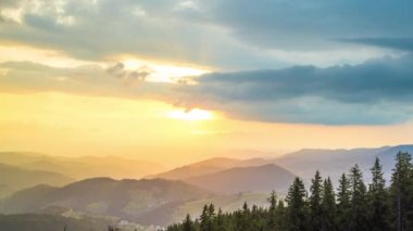 A mountain valley with mountain peaks of the Rhodope Mountains covered with dense spruce dark forests is shaded under a cloudy evening sunset bright sunny sky. UHD 4K video timelaps