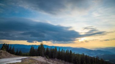 A mountain valley with mountain peaks of the Rhodope Mountains covered with dense spruce dark forests is shaded under a cloudy evening sunset bright sunny sky. UHD 4K video timelaps