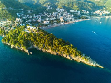 Birds eye view of historical resort towns of Budva and Becici with luxury hotels and comfortable beaches near azure calm Adriatic Sea against the backdrop of the Montenegrin Mountains and blue sky