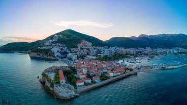 Panorama of sea port with small ships and boats for excursions on the Adriatic Sea near the ancient historical island of St. Stevan in the evening sunset city of Budva against a romantic cloudy sky