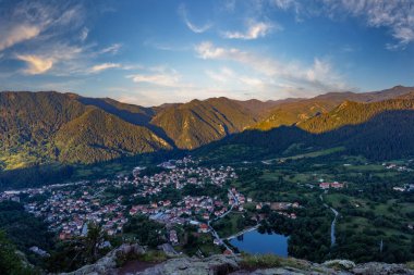 View from high rock to old village Smolyan with green meadows for cattle walking and houses, between mountain range of Rhodope Mountains sheltered by spruce forests