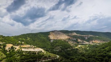 Industrial quarry for extraction of minerals with equipment and machines, and intermountain winding road passing by, in Rhodope Mountains covered with coniferous forests. UHD 8K video timelaps