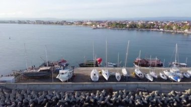A small sea fishing port with boats in the calm deep cool Black Sea adjoins the ancient resort small town of Pomorie in Bulgaria, under a blue cloudy sky. UHD 4K video realtime