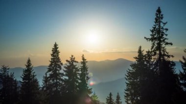 A mountain valley with mountain peaks of the Rhodope Mountains covered with dense spruce dark forests is shaded under a cloudy evening sunset bright sunny sky. UHD 8K video timelaps