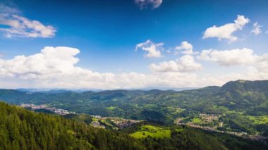 Unusual white fluffy clouds float across the blue evening sky with sunlight over the mountain valley of the Rhodope Mountains with the small village of Smolyan in the intermountain. UHD 8K video