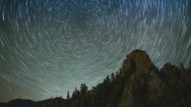 Rocky steep peak of a high mountain with dense dark spruce forests on the slopes against the backdrop of a magical starry clear night sky. UHD 8K video timelaps