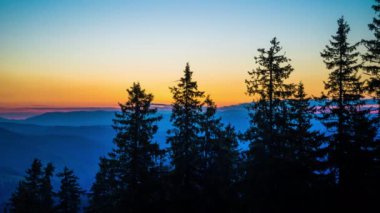 A mountain valley with mountain peaks of the Rhodope Mountains covered with dense spruce dark forests is shaded under a cloudy evening sunset bright sunny sky. UHD 8K video timelaps