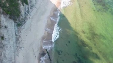 A wild empty sandy beach between a rocky sharp large ledge, covered with green fresh new vegetation, and a deep calm cool Black Sea under a clear blue sky. UHD 4K video realtime