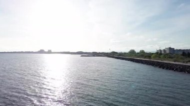 Sea promenade with people walking near the deep calm cool Black Sea, against the backdrop of the ancient resort small town of Pomorie in Bulgaria under a cloudy soft blue sky. UHD 4K video realtime