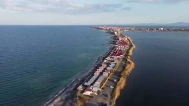 Kuşlar, Bulgaristan 'da açık mavi gökyüzü altında dalgalanan derin turkuaz Karadeniz' le çevrili kuru yabani çimenler ve küçük eski evlerle dar kumlu ve kayalık sahile bakıyor. UHD 4K video gerçek zamanlı