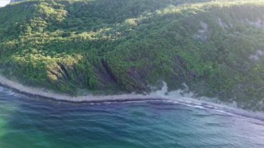 A wild empty sandy beach between a rocky sharp large ledge, covered with green fresh new vegetation, and a deep calm cool Black Sea under a clear blue sky. UHD 4K video realtime