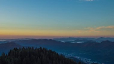 Cloudy weather over low hills covered with spruce evergreen forests in Rhodope Mountains against backdrop of sunset sky, and mystical thick white fog between mountain ranges. UHD 4K video timelaps