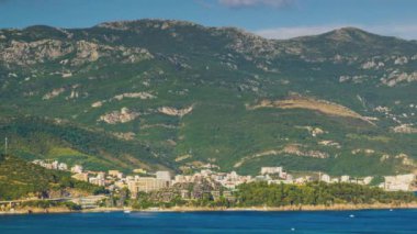 The steep slopes of the Montenegrin Mountains with resort hotels, tourist historical sites and summer green vegetation are washed by calm blue dark waters of the Adriatic Sea. UHD 4K video timelaps