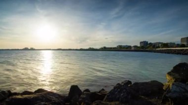 The embankment with rocky small dark stones passes over the bay of a calm deep Black sea against the backdrop of a sunset evening sunny sky. UHD 4k video timelaps