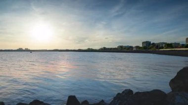The embankment with rocky small dark stones passes over the bay of a calm deep Black sea against the backdrop of a sunset evening sunny sky. UHD 4k video timelaps