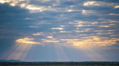 Bright sunset rays of the sun shine through thick evening white clouds over the blue calm Black Sea. UHD 4k video timelaps