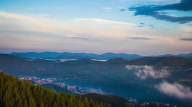 Green spring mountain valley sheltered by vegetation and spruce dark forests with small old village Smolyan, with grassy meadows where hungry motley sheep graze. UHD 4K video timelaps
