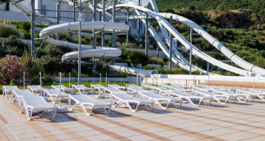 Empty indoor mountain summer water park with high extreme winding white slides and white folded sun loungers in spaced rows