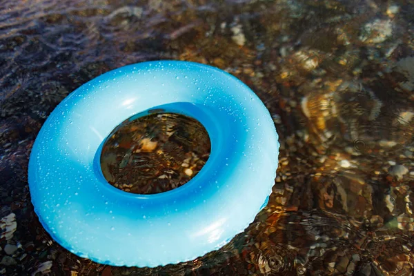 A small bright lost inflatable ring of blue color floats alone in the empty transparent blue Adriatic Sea in the evening