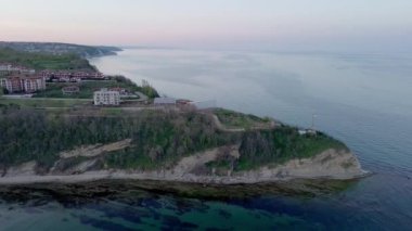 A small ancient resort town with expensive remote comfortable hotels on rocky outskirts, above a sandy vegetative wild beach near the deep blue Black Sea under a clear blue sky. UHD 4K video realtime