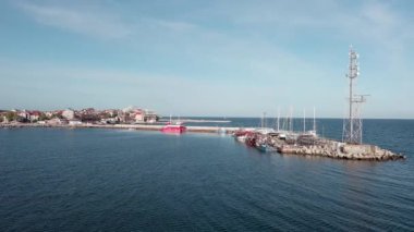 A small sea fishing port with boats in the calm deep cool Black Sea adjoins the ancient resort small town of Pomorie in Bulgaria, under a blue cloudy sky. UHD 4K video realtime