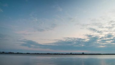 Bright sunset rays of the sun shine through thick evening white clouds over the blue calm Black Sea. UHD 4k video timelaps