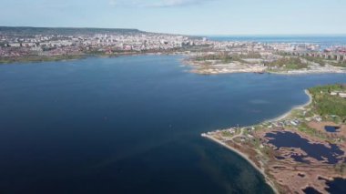 Koyu mavi Karadeniz, açık mavi bulutlu bir gökyüzünün altında geniş yeşil yolları ve büyük beton bir yol köprüsü olan bir sanayi kentini yıkıyor. UHD 4K video gerçek zamanlı