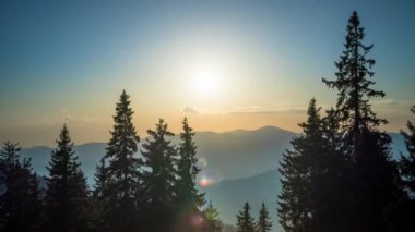 A mountain valley with mountain peaks of the Rhodope Mountains covered with dense spruce dark forests is shaded under a cloudy evening sunset bright sunny sky. UHD 4K video timelaps