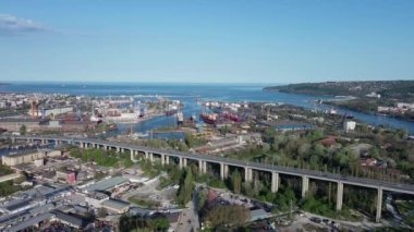 Large road bridge with trendy modern powerful cars passes over strait of Black Sea in ancient industrial city of Varna, with summer small hotels and inns and green spring parks. UHD 4K video realtime