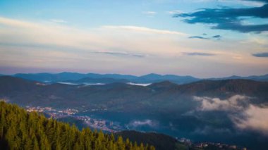 Green spring mountain valley sheltered by vegetation and spruce dark forests with small old village Smolyan, with grassy meadows where hungry motley sheep graze. UHD 8K video timelaps