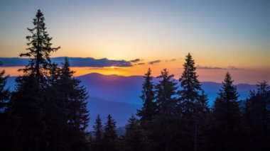 A mountain valley with mountain peaks of the Rhodope Mountains covered with dense spruce dark forests is shaded under a cloudy evening sunset bright sunny sky. UHD 8K video timelaps