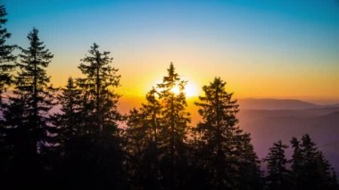 A mountain valley with mountain peaks of the Rhodope Mountains covered with dense spruce dark forests is shaded under a cloudy evening sunset bright sunny sky. UHD 8K video timelaps