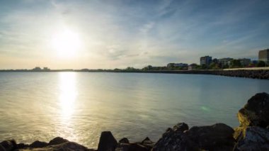 The embankment with rocky small dark stones passes over the bay of a calm deep Black sea against the backdrop of a sunset evening sunny sky. UHD 4k video timelaps
