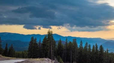 A mountain valley with mountain peaks of the Rhodope Mountains covered with dense spruce dark forests is shaded under a cloudy evening sunset bright sunny sky. UHD 4K video timelaps