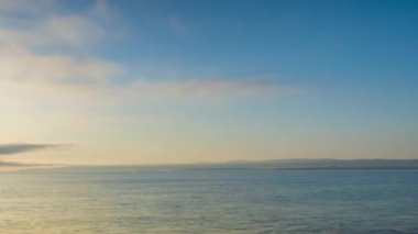 Calm blue boundless Black Sea with cool water reflecting light and sandy wild empty beach nearby, against cloudy colored sky with white clouds and bright dawn sun. UHD 4K video timelaps