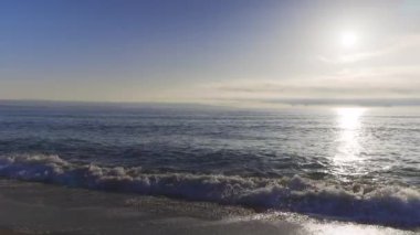 Calm blue boundless Black Sea with cool water reflecting light and sandy wild empty beach nearby, against cloudy colored sky with white clouds and bright dawn sun. UHD 8K video timelaps