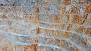 A natural stepped quarry rich in minerals is located near winding road, against backdrop of Rhodope Mountains and hills with evergreen spruce forests and mountain vegetation. UHD 4K video realtime