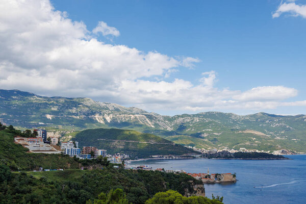 Birds eye view of historical resort towns of Budva and Becici with luxury hotels and comfortable beaches near azure calm Adriatic Sea against the backdrop of the Montenegrin Mountains and blue sky